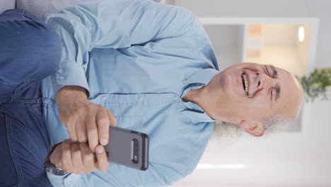 Vertical-video-of-Old-man-laughing-at-phone-message.